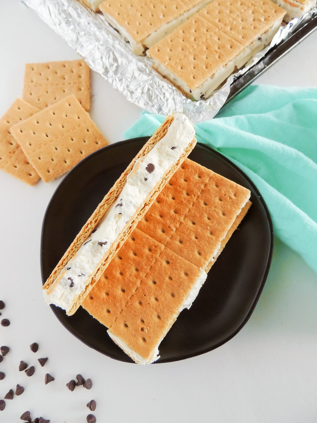 Homemade chocolate chip ice cream sandwiches on a blac plate near a green napkin.