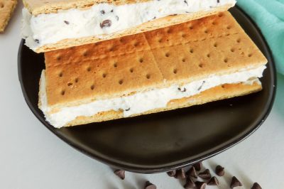 Homemade chocolate chip ice cream sandwiches on a blac plate near a green napkin.