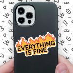 white man's hands holding a black iPhone case with Everything Is Fine sticker on it