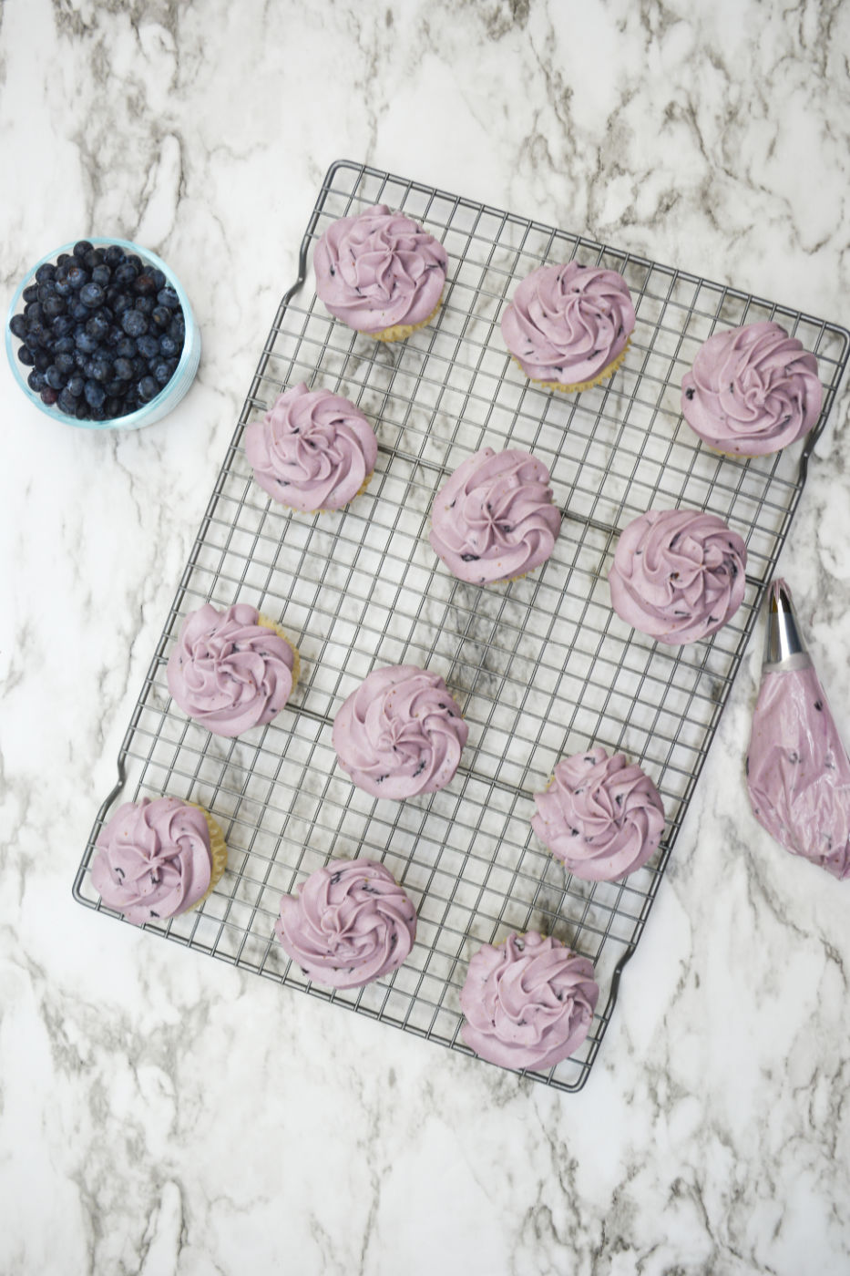 Cooling rack topped with frosted blueberry cupcakes