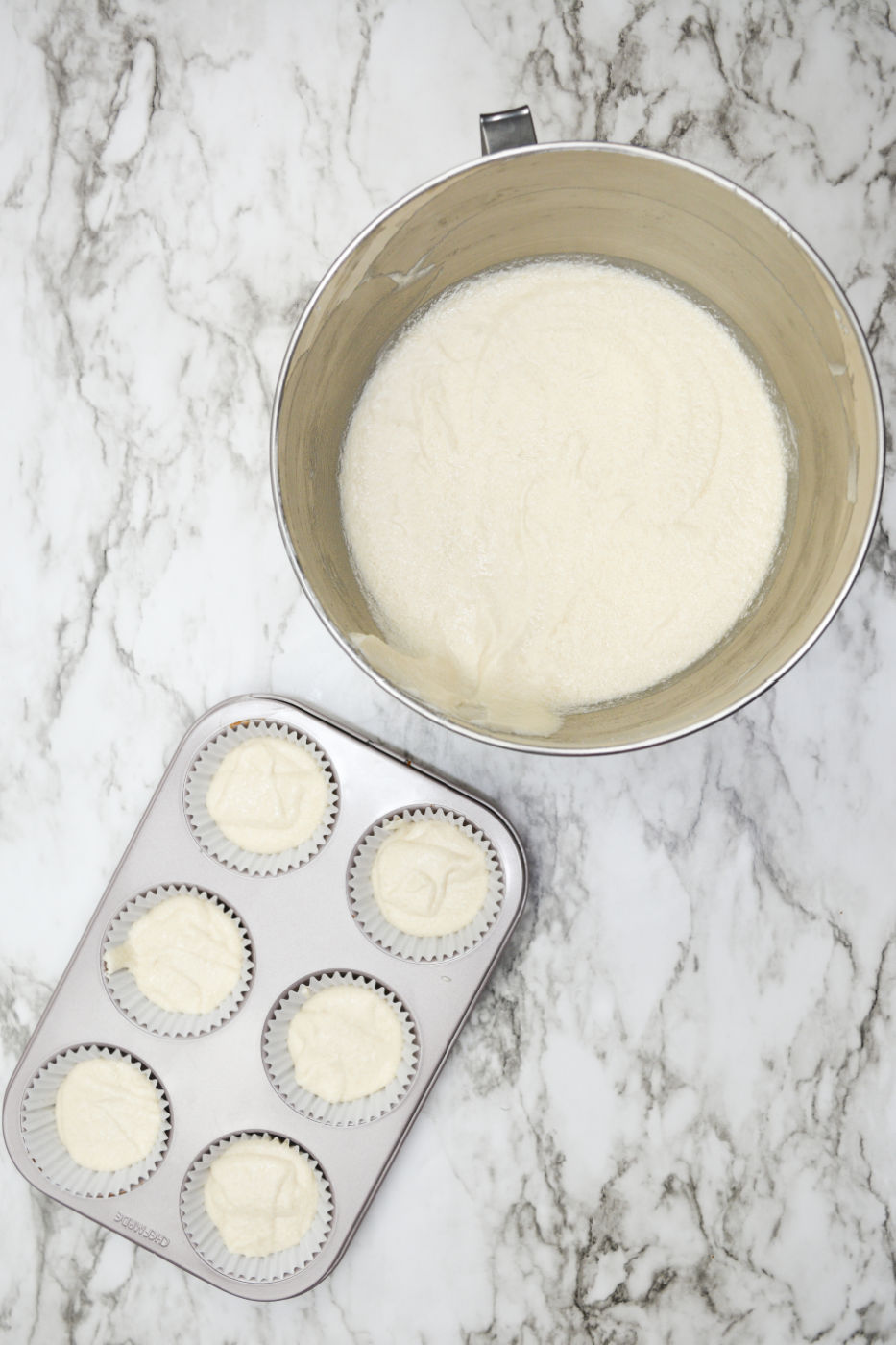 Mixing bowl filled with cupcake batter. Small cupcake can tin also filled with batter.