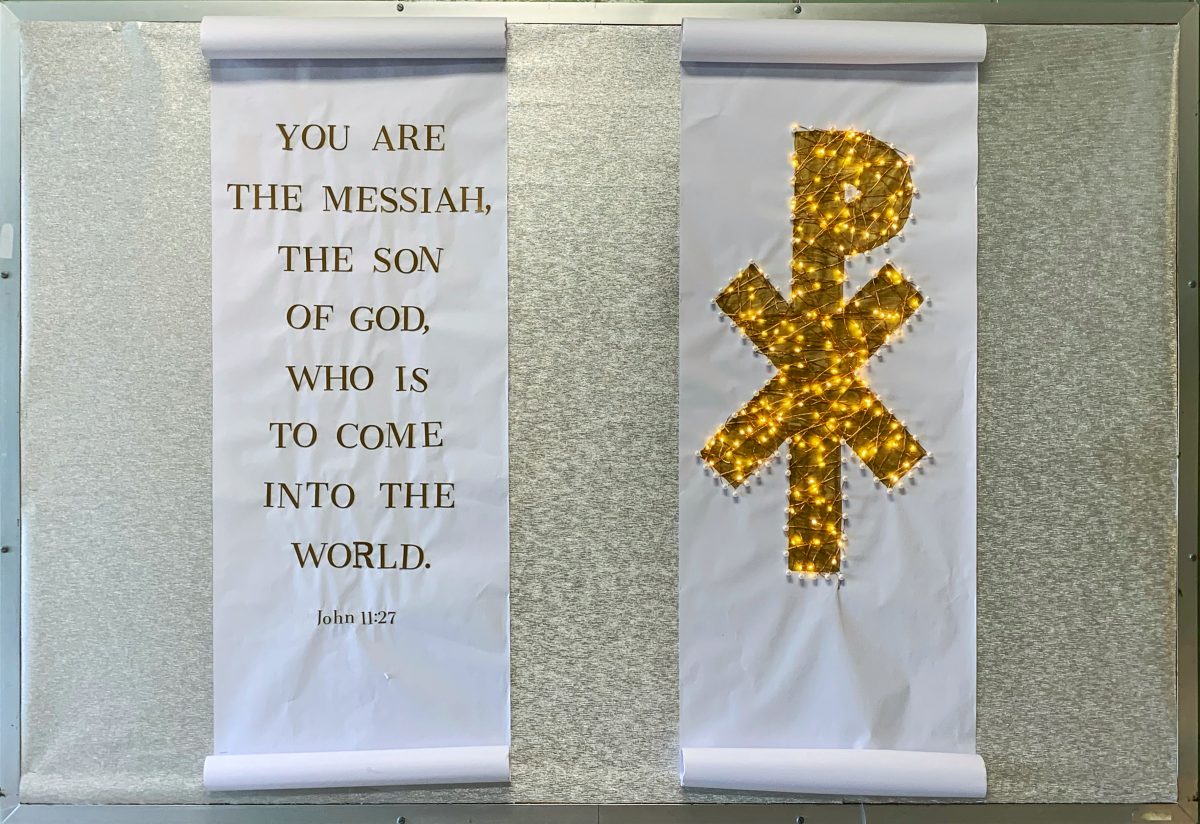 Silver bulletin board with two scrolls. One has a Bible verse and the other has a light up Chi Rho symbol