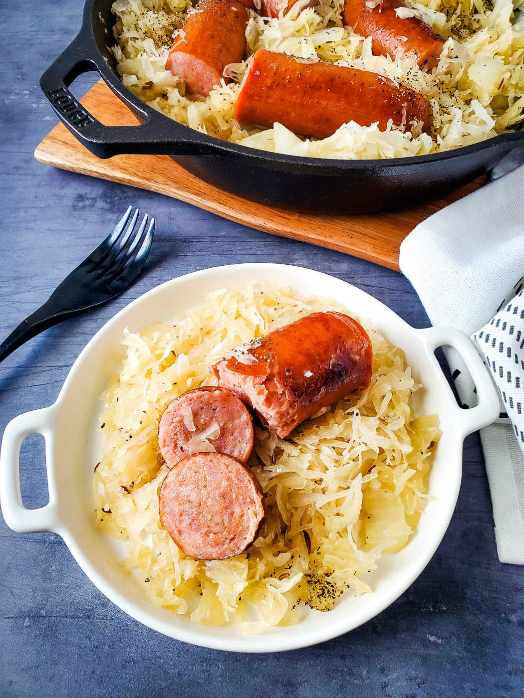 serving dish with sauerkraut and sausage near a cast iron skillet