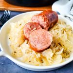close up of serving dish with sauerkraut and sausage near a cast iron skillet