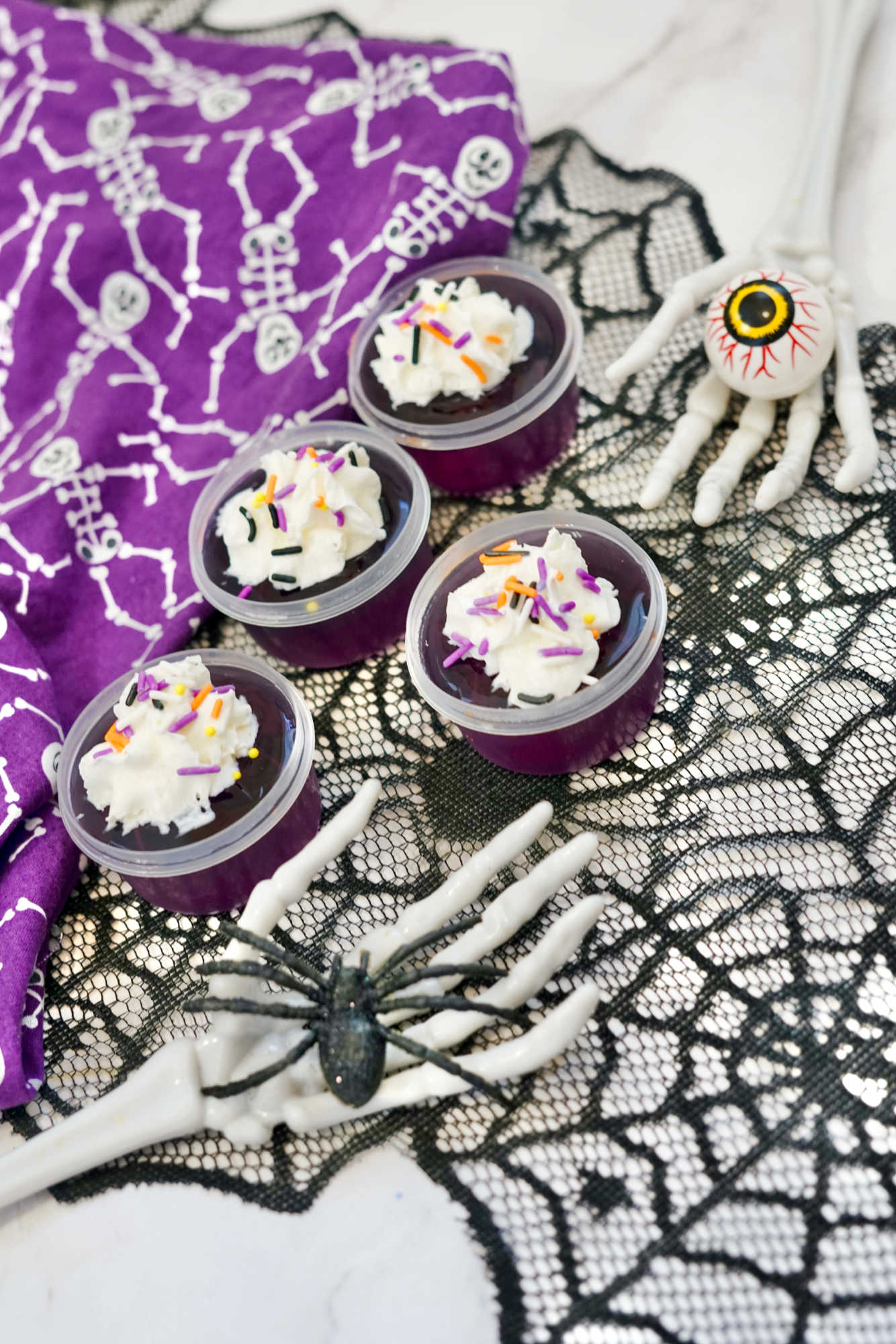 close up of purple jello shots topped with whipped cream near Halloween decor
