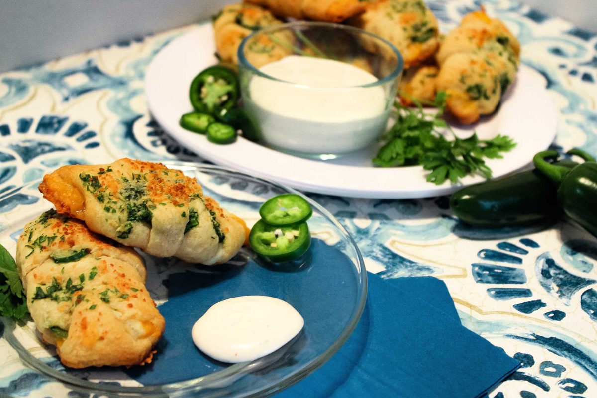 two cheesy jalapeno crescent rolls on a clear glass plate near a serving dish with more rolls