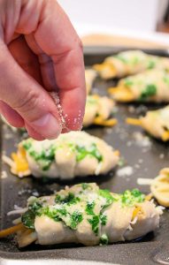 white woman's hand sprinkling parmesan cheese on the crescent rolls