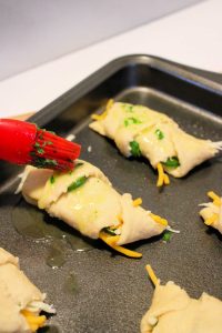 basting brush applying butter to cheesy jalapeno crescent rolls