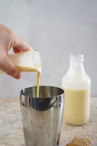 white woman's hand pouring eggnog into a cocktail shaker