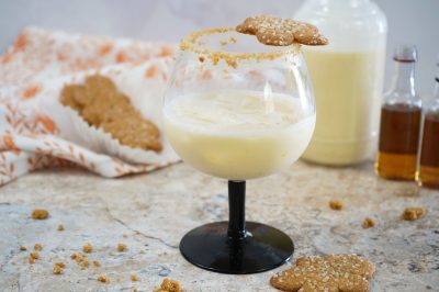 gingerbread man cookie balanced on a gingerbread cocktail near a bottle of eggbog