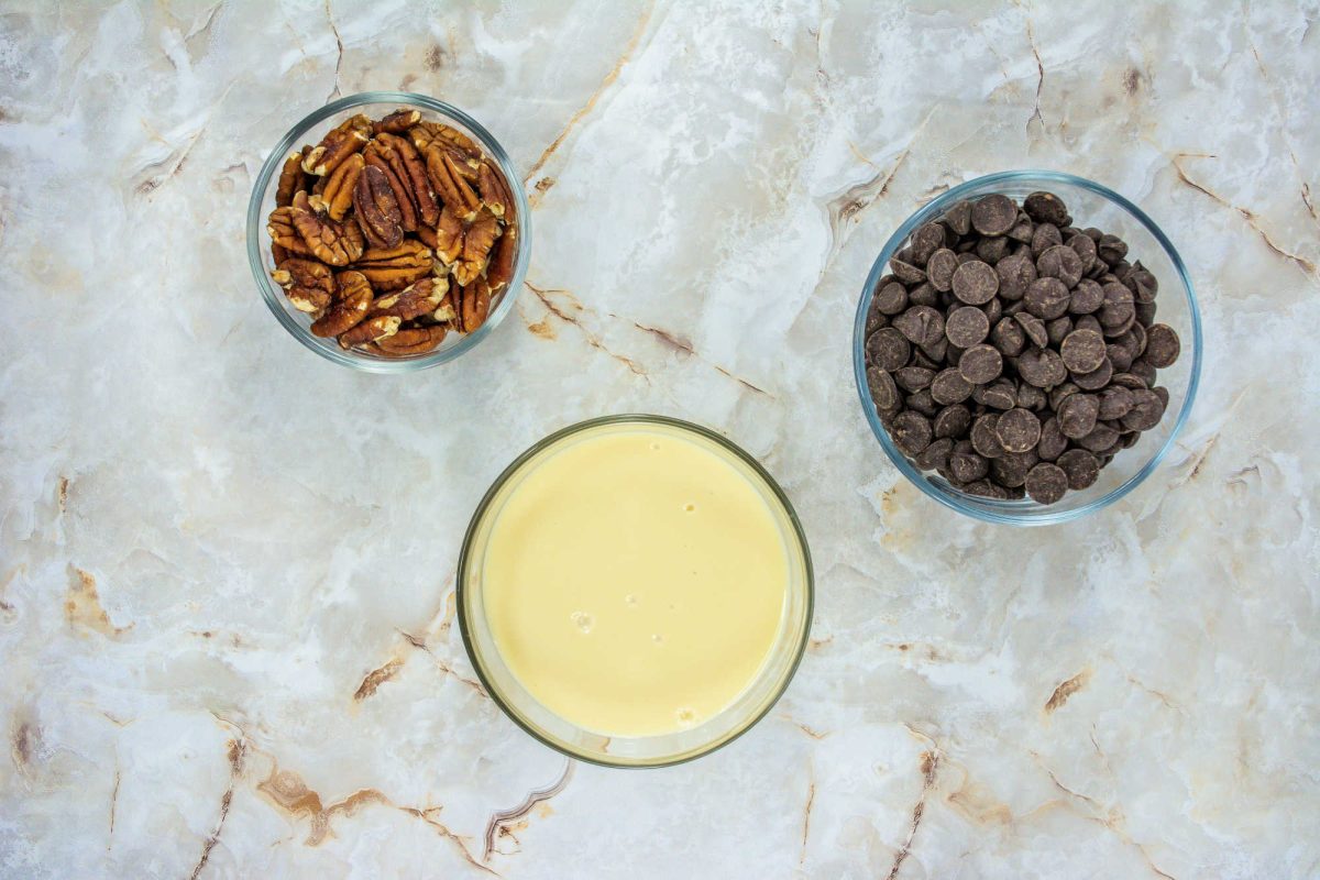 three small bowls containing pecans, sweetened condensed milk, and chocolate chips