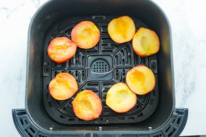 air fryer basket containing eight fresh peach halves