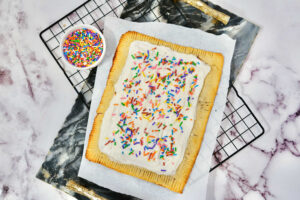 baked and frosted giant pop tart on a cutting board near a bowl of sprinkles