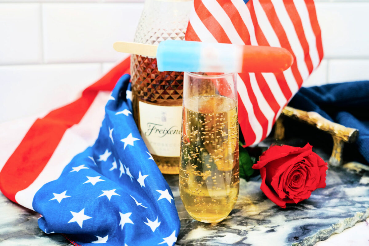 a bomb pop sitting on top of a flute of champagne near 4th of July decor