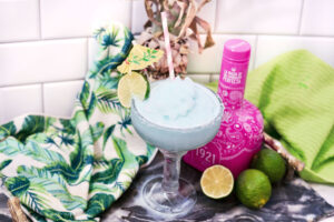 frozen blue margarita garnished with a lime slice near a bottle of tequila