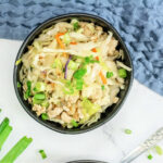 horizontal top view of egg roll in a bowl in a black bowl near green onions