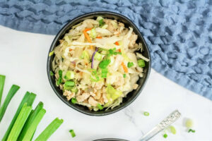 horizontal top view of egg roll in a bowl in a black bowl near green onions