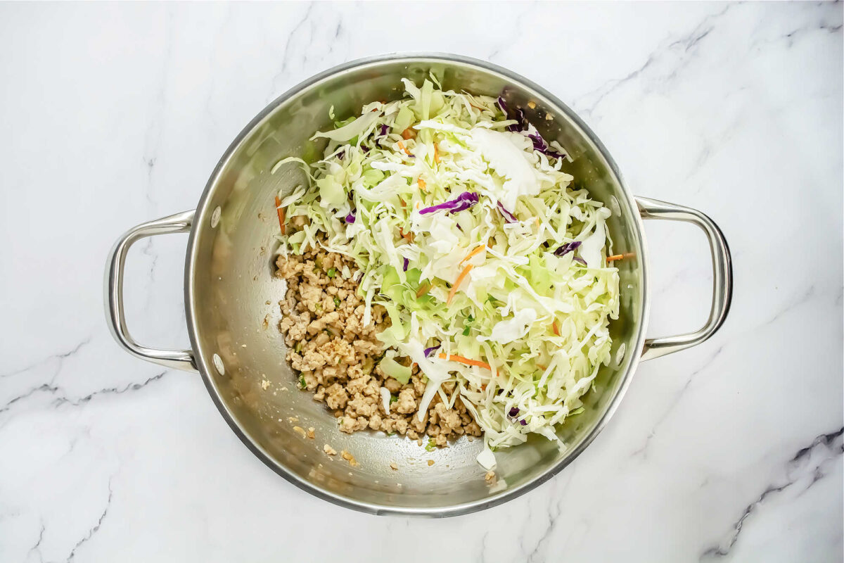 top view of ground turkey, green onion, garlic and cabbage in a wok