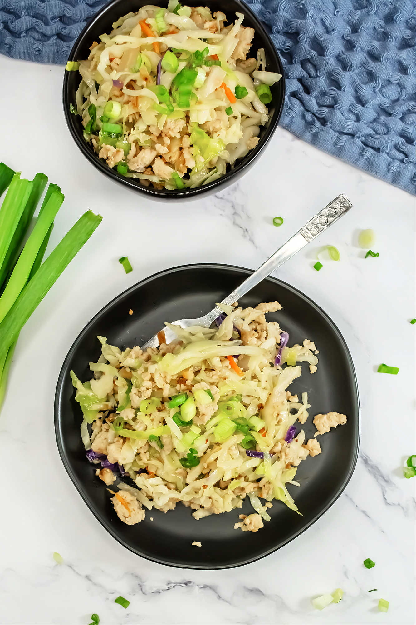 top view of 2 black bowls of egg roll in a bowl near green onions