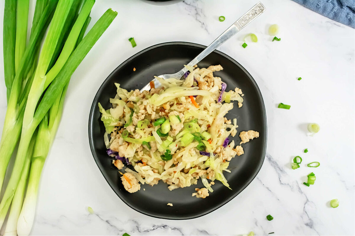 top view of egg roll in a bowl in a black bowl near green onions