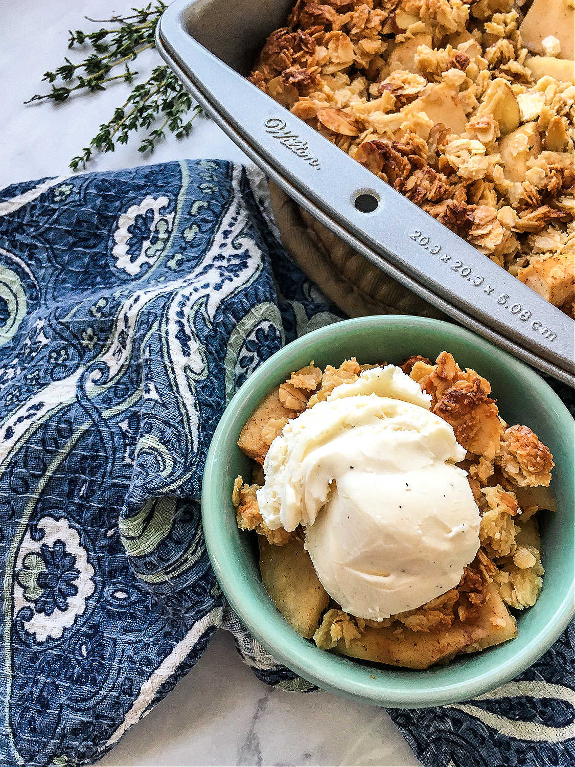 A green bowl full of apple crisp topped with vanilla ice cream near a blue napkin