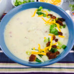 side view of a bowl of loaded baked potato soup garnished with bacon, cheese, and green onions