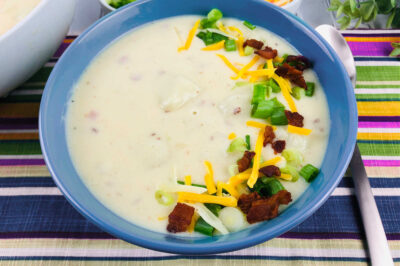 side view of a bowl of loaded baked potato soup garnished with bacon, cheese, and green onions