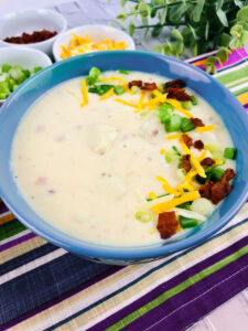 close p of a bowl of loaded baked potato soup garnished with onions, cheese, and bacon