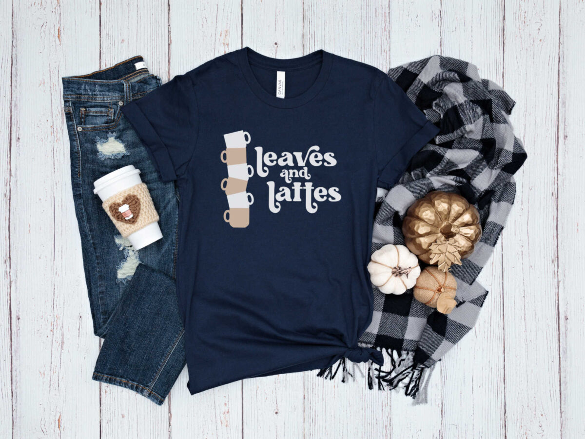 flat lay of a navy shirt with Leaves and Lattes design with jeans, a scarf, and a coffee cup