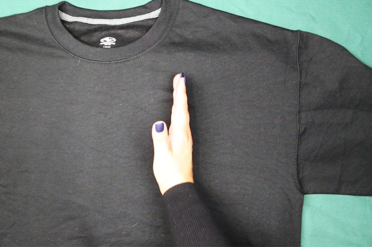 woman's hand indicating the left side of a sweatshirt neckline